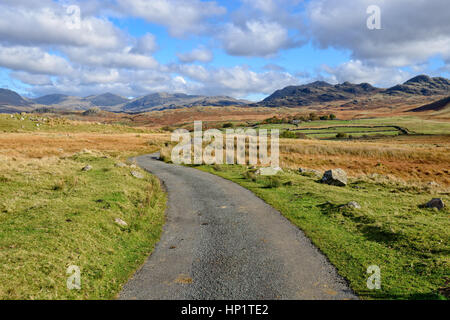 A winding country lane leading to mountains on Birker Fell in the Lake District National Park in Cumbria Stock Photo