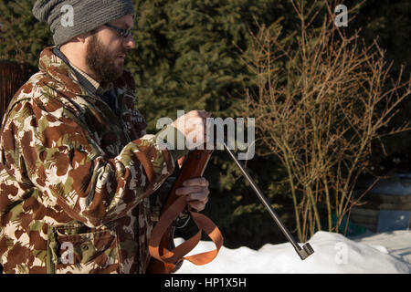 Man in winter forest reloads pneumatic weapons.  Hunter dressed in camouflage with pneumatic gun, rifle Stock Photo