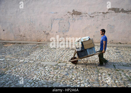 A Cuban man wheeling goods in a very old wooden wheelbarrow down a cobbled street in Trinidad Cuba Stock Photo