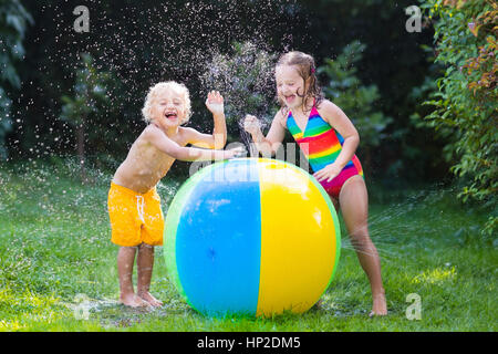 Child playing with toy ball garden sprinkler. Preschooler kid run and jump. Summer outdoor water fun in the backyard. Children play with hose watering Stock Photo
