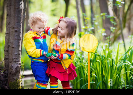 Children playing outdoors. Preschool kids catching frog with net. Boy and girl fishing in forest river. Adventure kindergarten day trip into wild natu Stock Photo