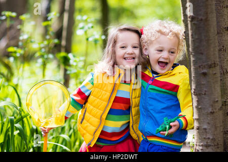 Children playing outdoors. Preschool kids catching frog with net. Boy and girl fishing in forest river. Adventure kindergarten day trip into wild natu Stock Photo