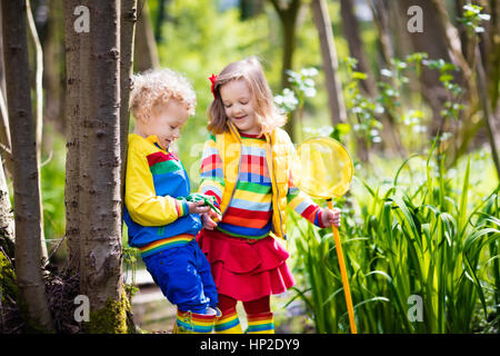 Children playing outdoors. Preschool kids catching frog with net. Boy and girl fishing in forest river. Adventure kindergarten day trip into wild natu Stock Photo