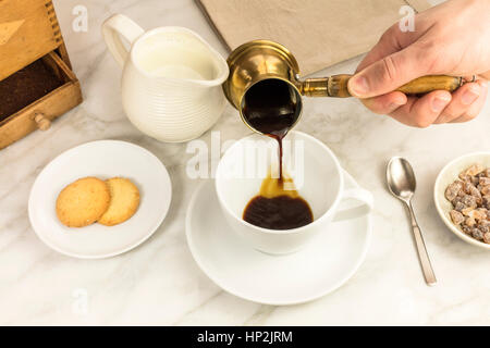 Coffee poured into a cup from a coffee pot, with a milk jar and cane sugar. Selective focus Stock Photo