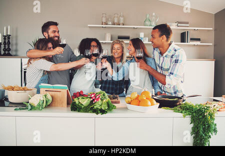 Group of young cheerful friends cheering while cooking some tasteful food at kitchen. Stock Photo