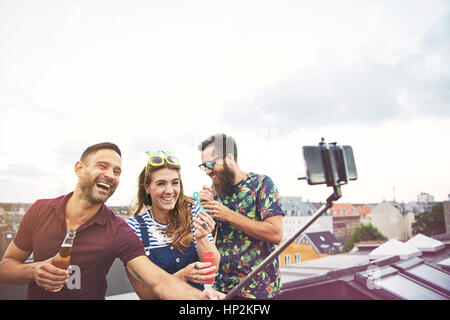 Three happy friends taking pictures of themselves on roof while drinking beer and blowing bubbles Stock Photo