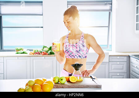 Young healthy woman standing in sunlight with glass of orange juice. Horizontal indoors shot Stock Photo