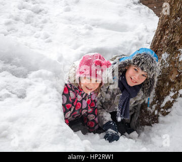 Happy boy and girl looking out from a snow cave they made in a snowdrift Stock Photo