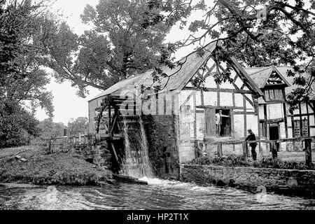 Edwardian watermill at work, miller standing in doorway. Kent, photographed in 1905. The miller is standing in the doorway talking to a second man who is leaning on the wooden fence. Restored from a high resolution scan taken from the original negative. Stock Photo