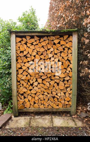 firewood - kiln-dried seasoned split hardwood logs for wood burning stove wood burner neatly stacked in small uk garden wood store Stock Photo