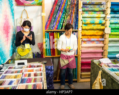 Two Japanese women in a fabric stall using their mobile telephones. Stock Photo