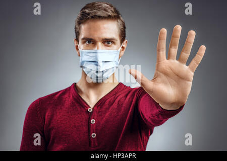 Handsome man showing gesture 'stop'. Photo of healthy man wears protective mask against infectious diseases and flu. Health care concept. Stock Photo