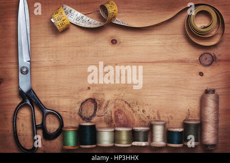 scissors, tape measure and old threads on old wooden background in vintage style (top view, toning) Stock Photo