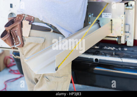 Worker Measuring An Aluminum Rain Gutter Feeding Through Seamless Shaping Machine. Stock Photo