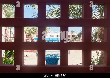 through Designer Grille seen tropical landscape with swimming pool and palm trees. Stock Photo