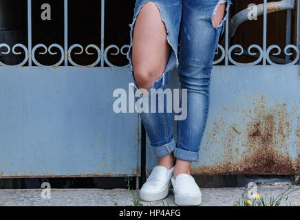female legs in torn jeans, close-up, against the background of openwork lattice Stock Photo