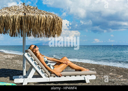 Beautiful young woman sunbathing on the beach in a lounge chair Stock Photo