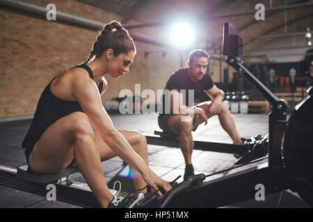 Young sportive woman and man sitting on rowing machines and having break. Stock Photo