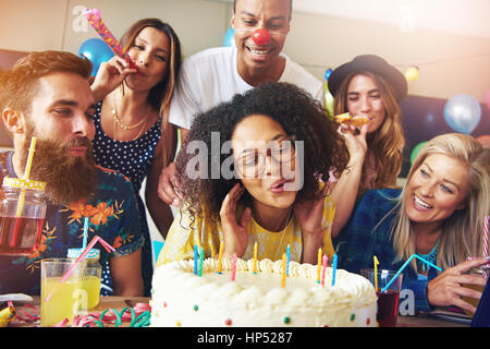 Happy woman blowing candles on cake while surrounded by friends at table for birthday or anniversary celebration Stock Photo