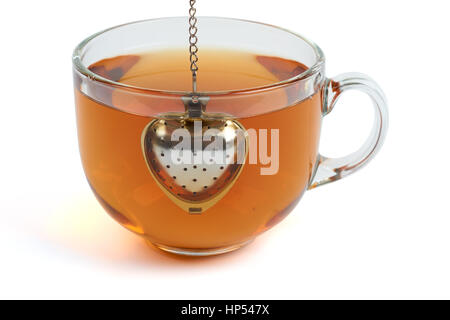 Brewing black tea in the transparent glass cup with heart shape tea strainer. Isolated on white Stock Photo
