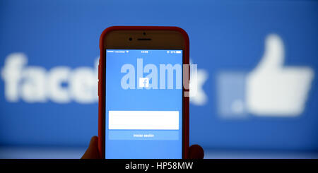 Hand holding a mobile phone with notifications picture on it. Facebook's logo is shown on the background in a monitor. Stock Photo