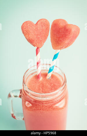 Watermelon smoothie in Mason jar decorated with watermelon heart slices on blue background Stock Photo