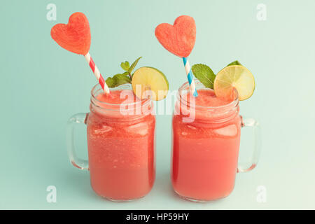 Sweet watermelon smoothie in Mason jars decorated with mint, lime and watermelon slices curved like heart symbols Stock Photo