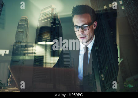 Optimistic businessman working on laptop at office in the night, Working overtime with big city in background Stock Photo