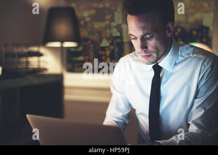 Businessman working on laptop at night sitting at office, big city in background, Overtime concept Stock Photo