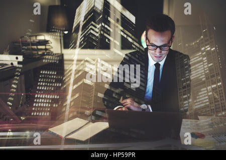 Optimistic businessman working on laptop at office in the night, Working overtime with big city in background Stock Photo