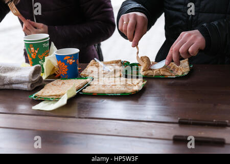 Moscow, Russia. Sunday, Feb. 19, 2017. Unidentified, unrecognizable people eat fresh hot pancakes on Manege square.  Maslenitsa, pancake, cheese fare week festival, carnival started in the city. People enjoy street performances and eat hot pancakes. This is also farewell to winter festival. The day is warm (+2C, about 36F) but gloomy. © Alex's Pictures/Alamy Live News Stock Photo