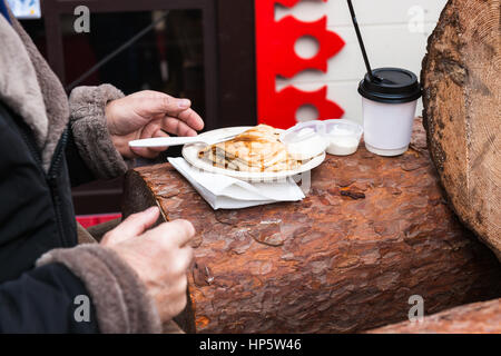 Moscow, Russia. Sunday, Feb. 19, 2017. Unidentified, unrecognizable people eat fresh hot pancakes on Manege square.  Maslenitsa, pancake, cheese fare week festival, carnival started in the city. People enjoy street performances and eat hot pancakes. This is also farewell to winter festival. The day is warm (+2C, about 36F) but gloomy. © Alex's Pictures/Alamy Live News Stock Photo