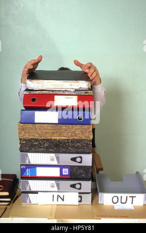 businessman hidden behind giant mound of paperwork in office Stock Photo
