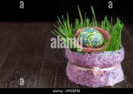 Easter egg and sprouts of wheat on the wooden surface. Low key, selective focus. Stock Photo