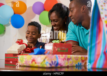 Happy black family at home. African american father, mother and child celebrating birthday, having fun at party. Young boy opening gifts and smiling. Stock Photo