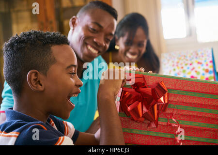 Happy black family at home. African american father, mother and child celebrating birthday, having fun at party. Young boy opening gifts and smiling. Stock Photo