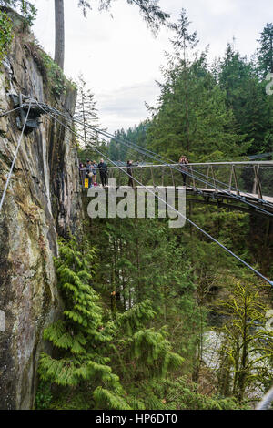 Vancouver, Canada - January 28, 2017: A suspension bridge hanging from a cliff face high above the canyon at the Capilano Suspension Bridge Park Stock Photo