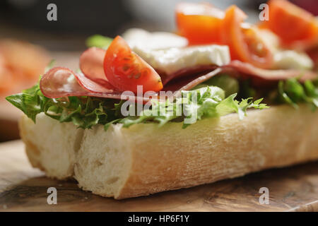 open sandwich with prosciutto, mozzarella and tomatoes on kitchen table, shallow focus Stock Photo