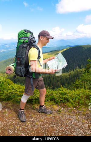 Man tourist in mountain read the map. Man on top of mountain. Tourism concept. Man with map in the hands of the traveler, the tourist on background of Stock Photo