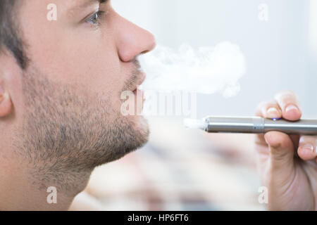 Young man smoking electronic cigarette. Closeup portrait of bearded man smoking an e-cigarette. Man vaping an electronic cigarette Stock Photo