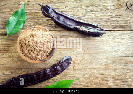 Carob pods and carob powder over wooden background with copy space - organic healthy ingredient for vegan vegetarian food and drinks Stock Photo