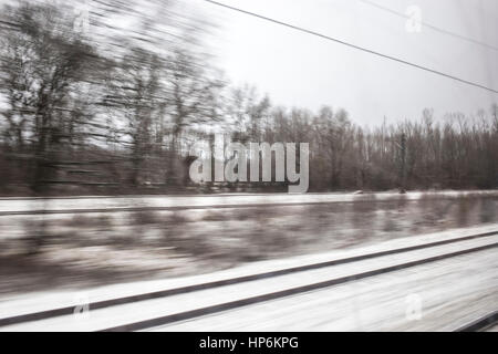 View from window of train travelling towards Amsterdam, Netherlands, with trees and snow in view. Stock Photo