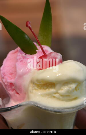 Strawberry and vanilla ice cream scoops in a glass bowl with cherry on top Stock Photo