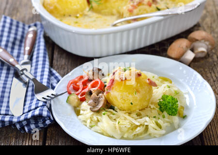 Hearty potato dumpling gratin with cheese and bacon served on warm coleslaw Stock Photo
