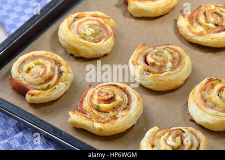 Baked hearty puff pastry rolls with ham, cream cheese, parmesan and herbs on a griddle Stock Photo