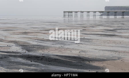 Sea coal washed up on Saltburn beach in winter, also showing the Victorian pier and Warsett Hill Stock Photo