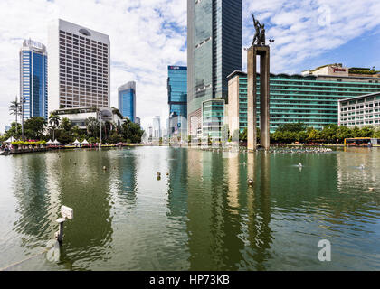 JAKARTA, INDONESIA - SEPTEMBER 25, 2016: Tall office buildings and luxury hotels reflect in the water of the fountain of the Selamat Datang monument i Stock Photo