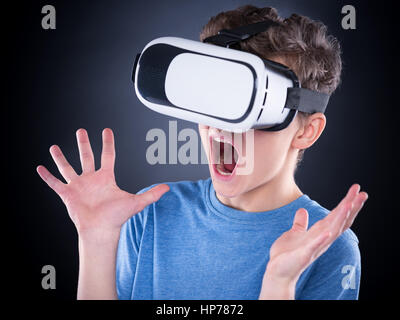 Amazed teen boy screaming, wearing virtual reality goggles watching movies or playing video games. Surprised teenager looking in VR glasses and shouti Stock Photo