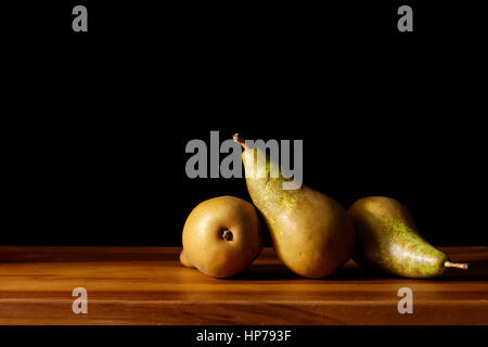 Study of three green conference pears arranged on a wooden surface with side lighting in painterly style with black background. Stock Photo