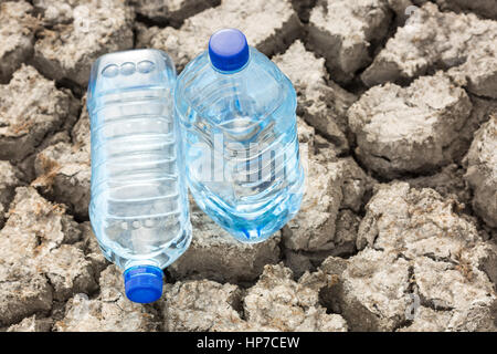 bottle with water on the dried ground close up. Global drought, warming. Stock Photo